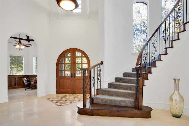 entrance foyer featuring ceiling fan, a healthy amount of sunlight, a towering ceiling, and french doors