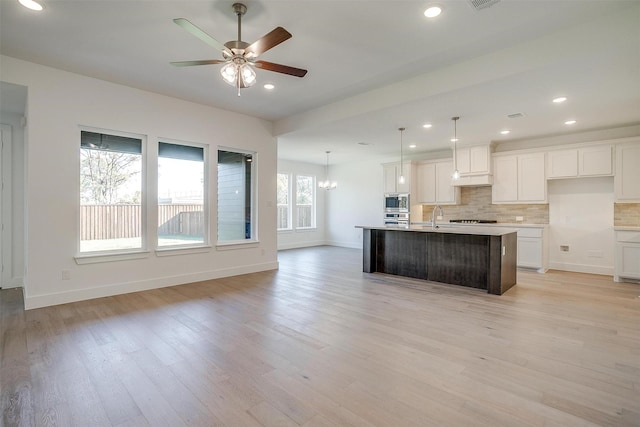 kitchen featuring sink, white cabinetry, appliances with stainless steel finishes, pendant lighting, and a kitchen island with sink