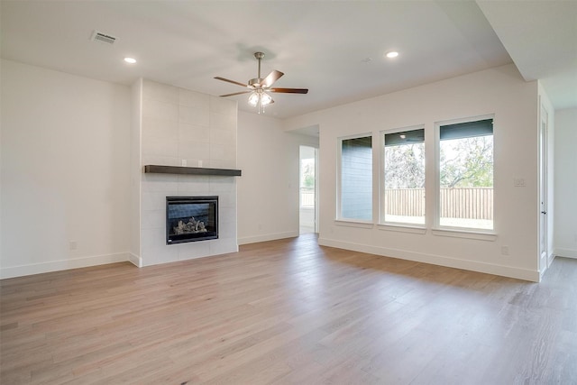 unfurnished living room featuring ceiling fan, a healthy amount of sunlight, a tiled fireplace, and light wood-type flooring