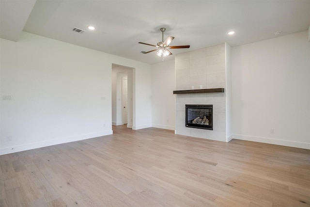 unfurnished living room with ceiling fan, a tiled fireplace, and light hardwood / wood-style floors