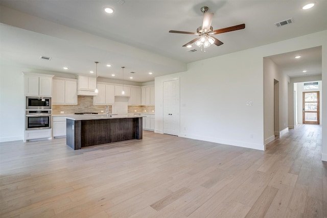 kitchen with white cabinetry, hanging light fixtures, backsplash, stainless steel appliances, and a center island with sink