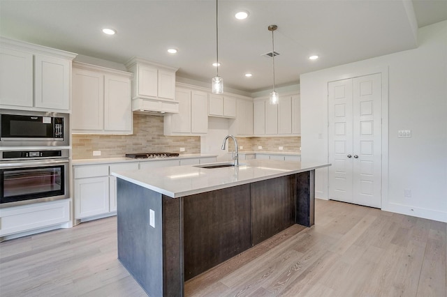 kitchen featuring sink, white cabinetry, appliances with stainless steel finishes, an island with sink, and pendant lighting