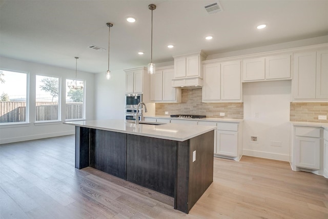 kitchen featuring an island with sink, sink, hanging light fixtures, and white cabinets