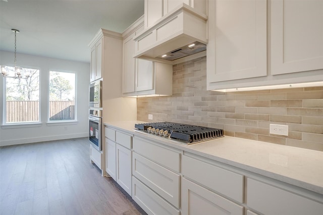 kitchen featuring premium range hood, hanging light fixtures, backsplash, stainless steel appliances, and light stone counters