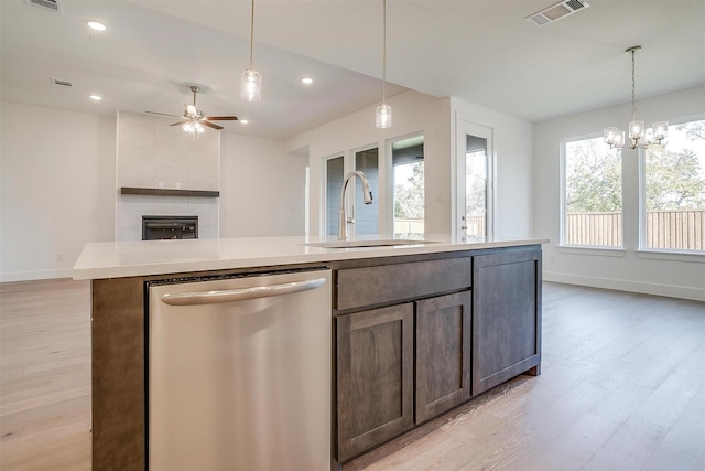 kitchen featuring an island with sink, sink, hanging light fixtures, stainless steel dishwasher, and light wood-type flooring