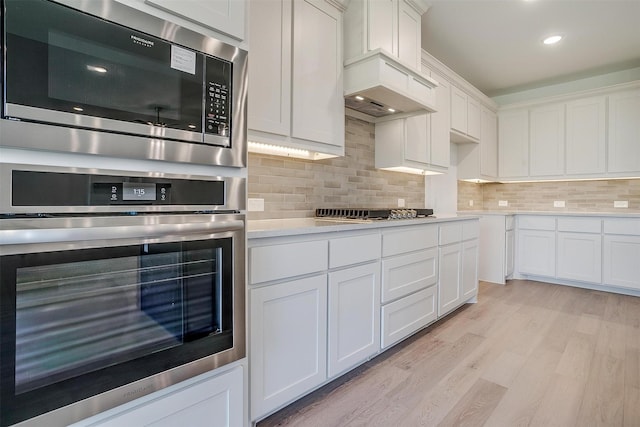 kitchen featuring stainless steel appliances, backsplash, white cabinets, and light wood-type flooring