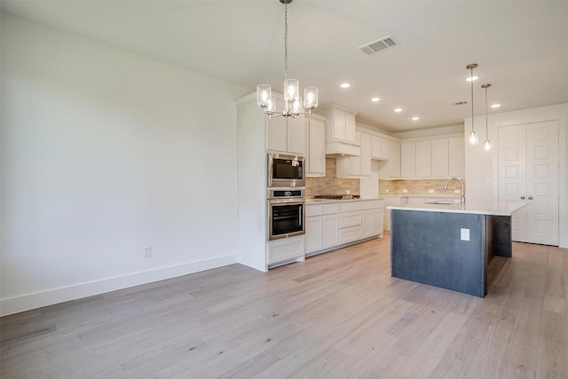 kitchen with a center island with sink, appliances with stainless steel finishes, pendant lighting, decorative backsplash, and white cabinets