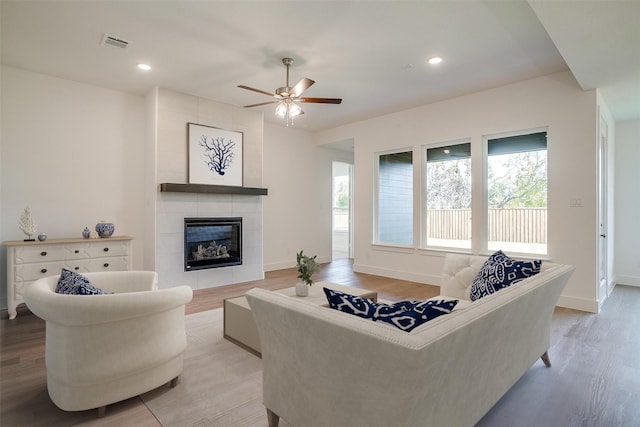 living room with hardwood / wood-style flooring, a tile fireplace, and ceiling fan