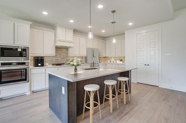 kitchen with sink, stainless steel appliances, white cabinets, a center island with sink, and decorative light fixtures