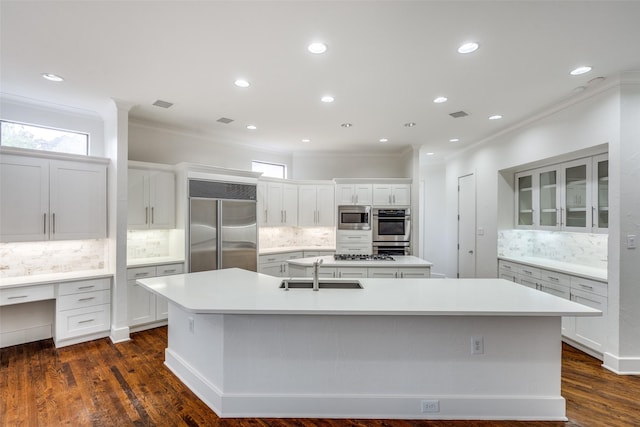 kitchen featuring sink, crown molding, built in appliances, a center island with sink, and white cabinets