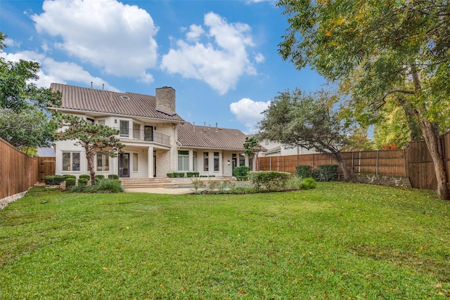 rear view of house with a balcony, a patio area, and a lawn