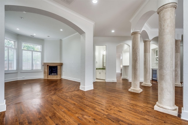 unfurnished living room with ornate columns, crown molding, and dark wood-type flooring