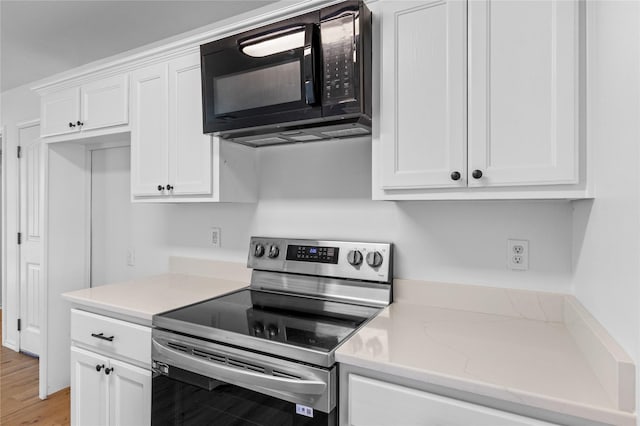 kitchen with stainless steel electric range oven, light stone countertops, white cabinets, and light hardwood / wood-style flooring