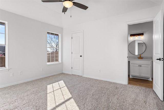 unfurnished bedroom featuring sink, ensuite bath, light colored carpet, and ceiling fan