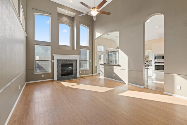 unfurnished living room with a towering ceiling, light wood-type flooring, and ceiling fan