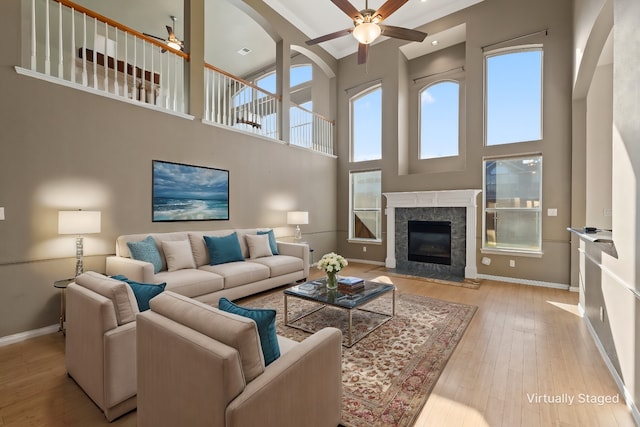 living room with a high ceiling, light hardwood / wood-style flooring, ceiling fan, and a premium fireplace