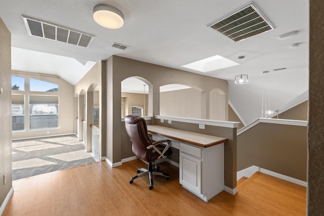 office with light wood-type flooring, built in desk, and vaulted ceiling with skylight