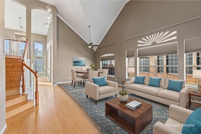 living room with ceiling fan with notable chandelier, light wood-type flooring, crown molding, and high vaulted ceiling