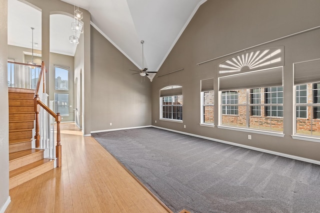 unfurnished living room with hardwood / wood-style floors, ceiling fan with notable chandelier, crown molding, and high vaulted ceiling