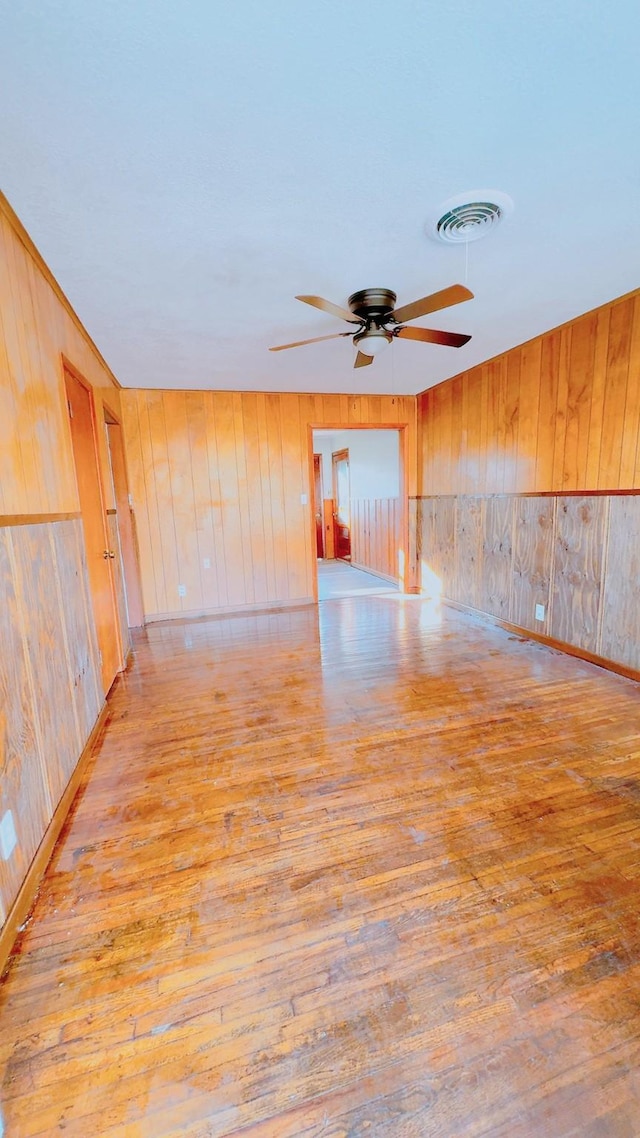 empty room with wood walls, ceiling fan, and light wood-type flooring