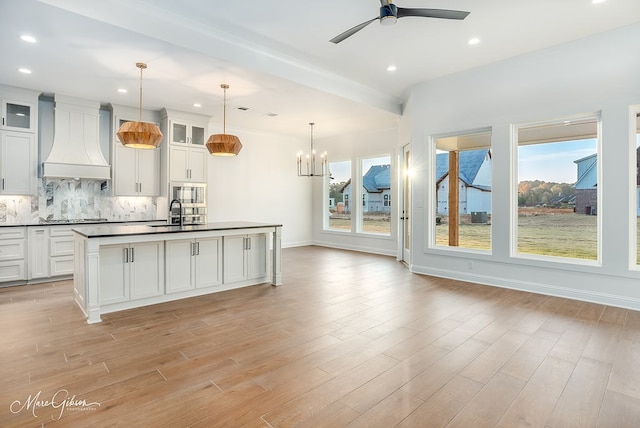 kitchen featuring dark countertops, backsplash, custom range hood, light wood-style flooring, and stainless steel gas stovetop