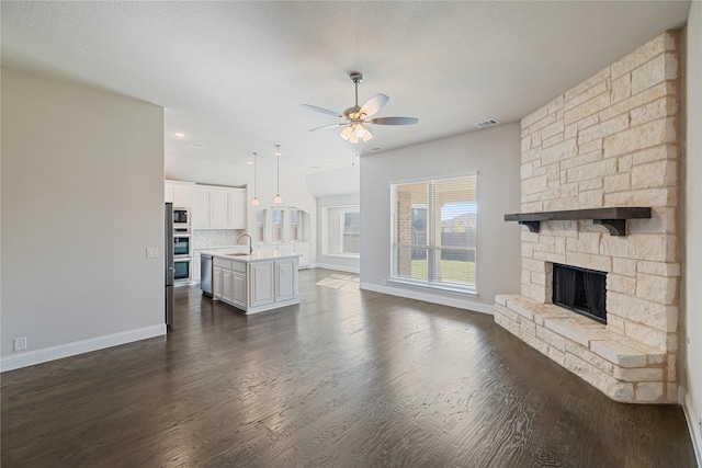 unfurnished living room with a fireplace, sink, ceiling fan, dark wood-type flooring, and a textured ceiling