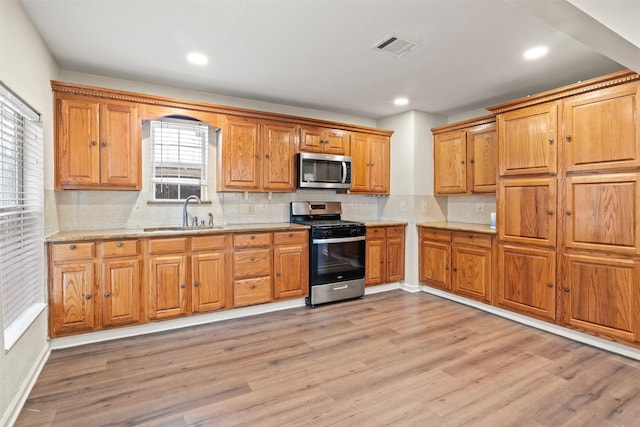 kitchen featuring tasteful backsplash, sink, stainless steel appliances, and light wood-type flooring