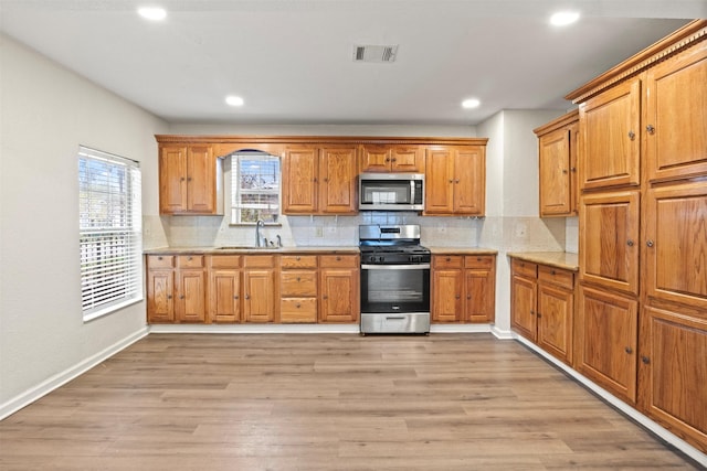 kitchen with backsplash, sink, light hardwood / wood-style floors, and appliances with stainless steel finishes