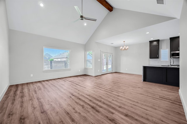 unfurnished living room featuring a healthy amount of sunlight, beam ceiling, light hardwood / wood-style floors, and ceiling fan with notable chandelier