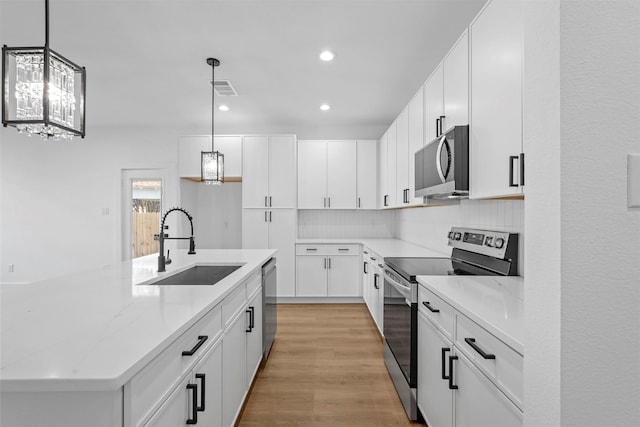 kitchen featuring stainless steel appliances, white cabinetry, hanging light fixtures, and sink