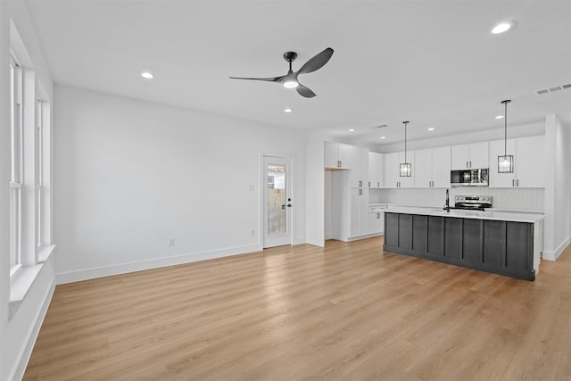 interior space with light hardwood / wood-style flooring, pendant lighting, a center island with sink, white cabinets, and appliances with stainless steel finishes