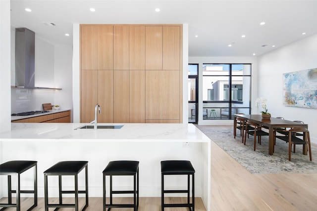 kitchen featuring a kitchen bar, wall chimney range hood, sink, kitchen peninsula, and light stone counters