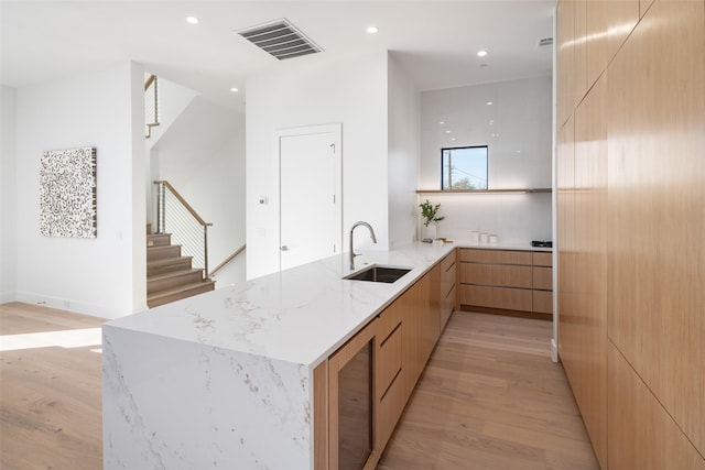 kitchen with light hardwood / wood-style floors, light stone countertops, sink, kitchen peninsula, and light brown cabinets