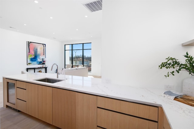 kitchen featuring sink, light hardwood / wood-style floors, light brown cabinetry, and light stone countertops