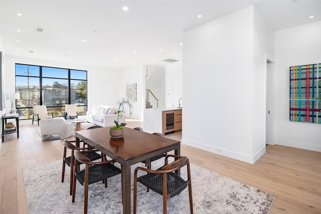 dining space with floor to ceiling windows, sink, beverage cooler, and light hardwood / wood-style flooring