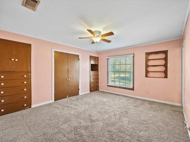 unfurnished bedroom with carpet flooring, ceiling fan, ornamental molding, and multiple closets