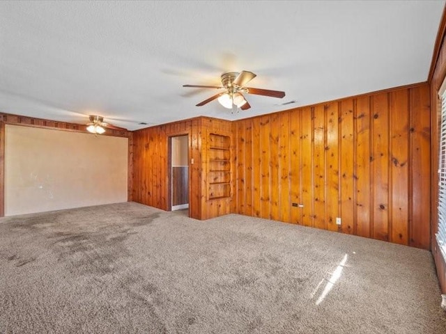 unfurnished room featuring ceiling fan, carpet flooring, and wood walls