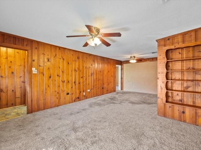 carpeted spare room with ceiling fan and wood walls