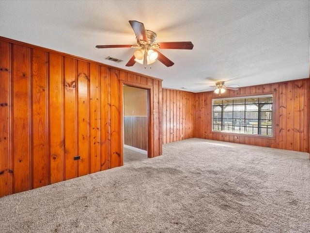 carpeted empty room featuring ceiling fan, a textured ceiling, and wood walls