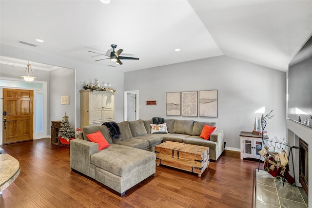 living room featuring ceiling fan, dark hardwood / wood-style flooring, a tiled fireplace, and vaulted ceiling