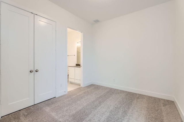 unfurnished bedroom with a closet, connected bathroom, and light carpet