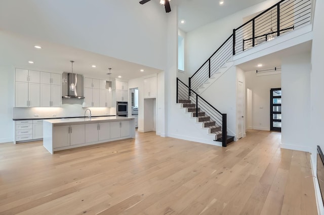 kitchen featuring white cabinets, decorative light fixtures, an island with sink, and wall chimney range hood