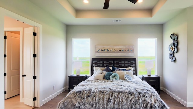 bedroom featuring a raised ceiling, hardwood / wood-style floors, and multiple windows