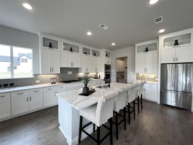 kitchen with stainless steel appliances, light stone countertops, an island with sink, and white cabinets