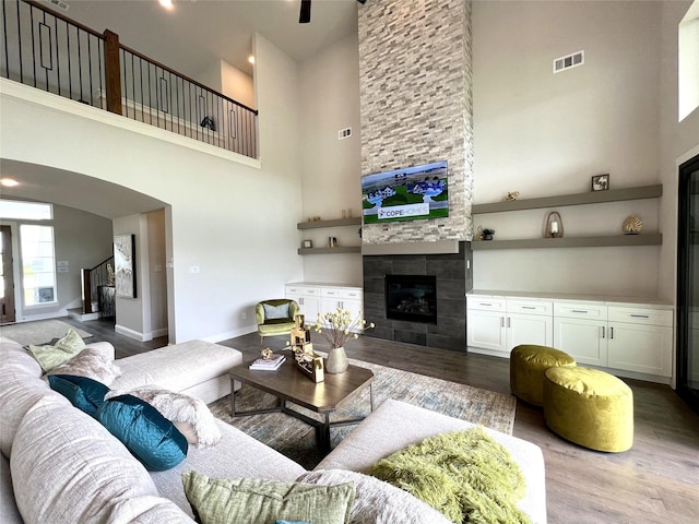 living room with hardwood / wood-style flooring, a towering ceiling, and a tiled fireplace