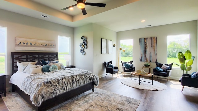 bedroom with ceiling fan, a tray ceiling, and light wood-type flooring