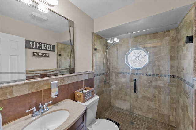 bathroom featuring a shower with door, vanity, tile walls, and toilet