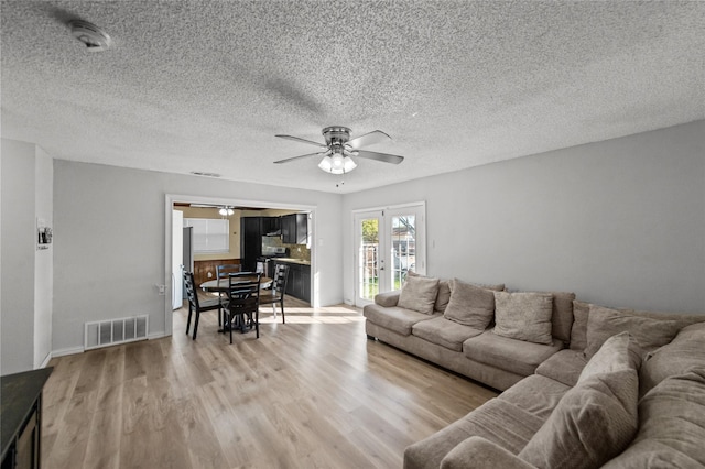 living room featuring french doors, a textured ceiling, light hardwood / wood-style flooring, and ceiling fan