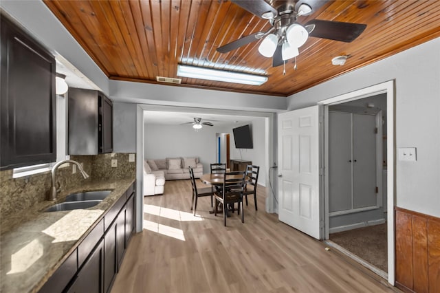 kitchen with decorative backsplash, light wood-type flooring, dark stone counters, sink, and wooden ceiling