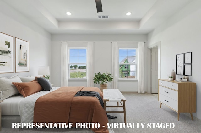 carpeted bedroom featuring a raised ceiling, multiple windows, and ceiling fan